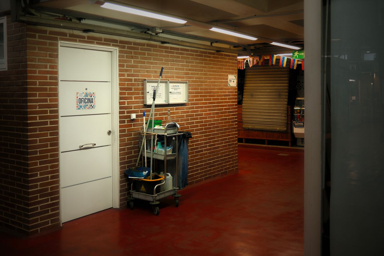 about-02 A brightly lit industrial hallway with a cleaning cart and supplies near an office door.