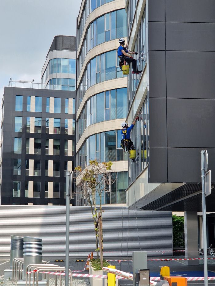 hero-img-01 Two workers clean windows on a tall office building in a city setting.